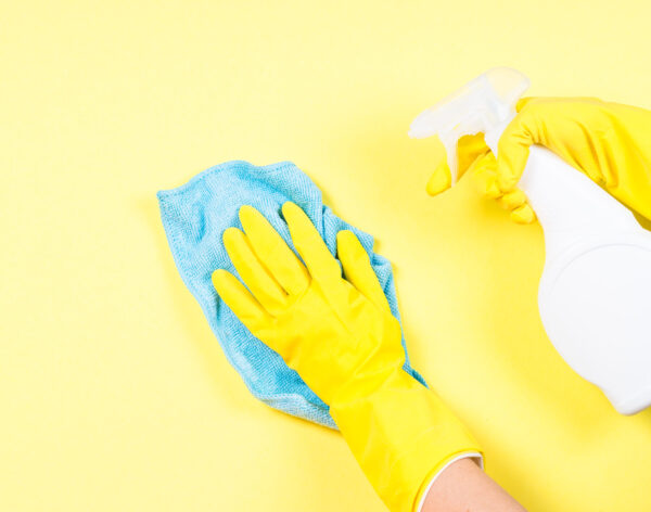 Woman cleaning yellow wall with microfiber rag, gloves and cleaning spray agent.