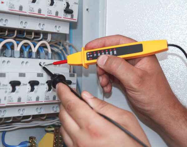Hands of electrician with multimeter probe at an electrical switchgear cabinet examining fuse box